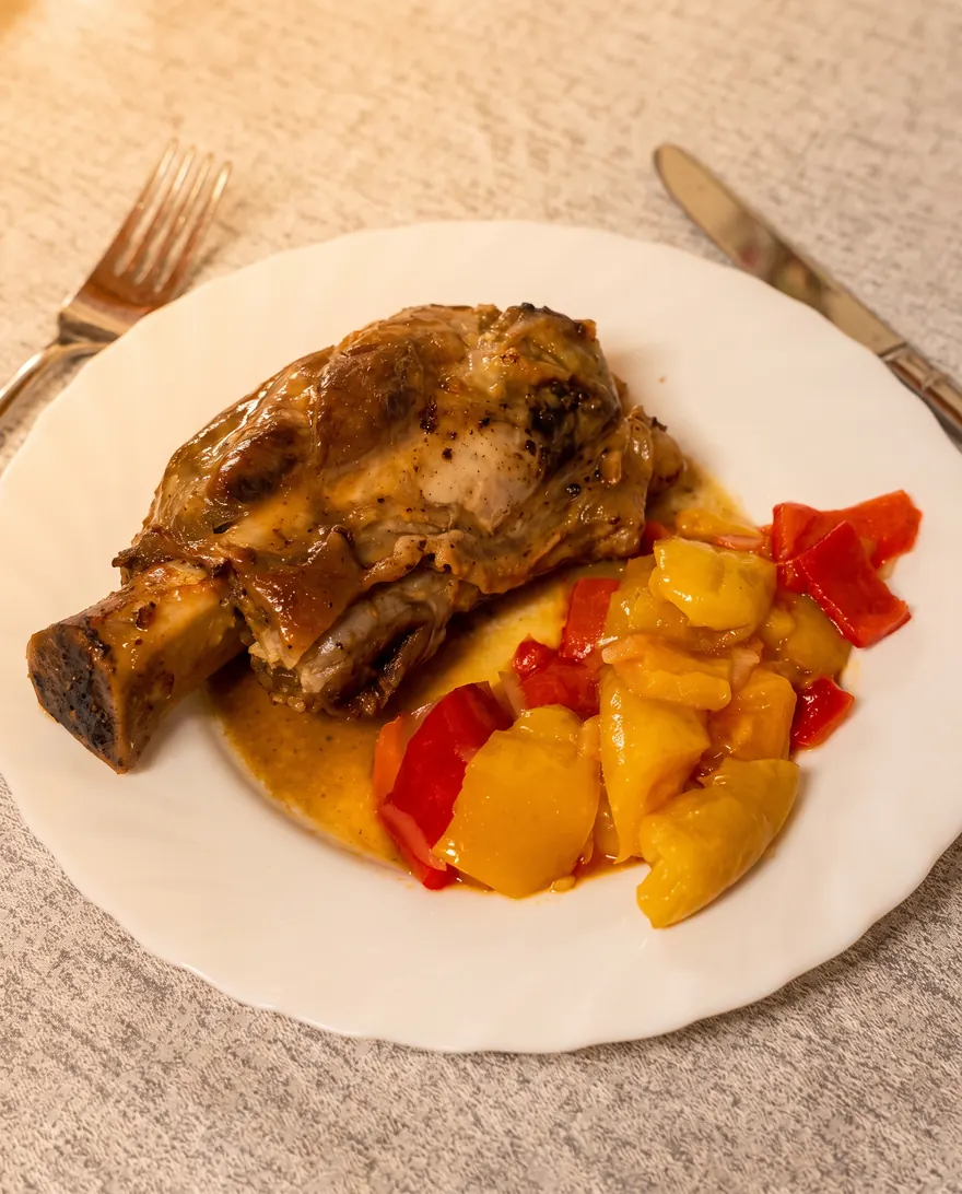 Stinco di maiale al forno con patate e peperoni.